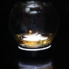 Glass bowl filled with found objects and a tiny sculpted figure embedded in resin lit from below in a dark space
